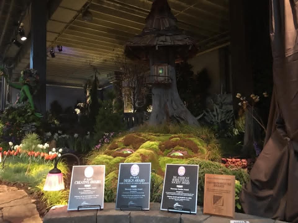 Four award plaques displayed in front of a fairy treehouse show garden exhibit
