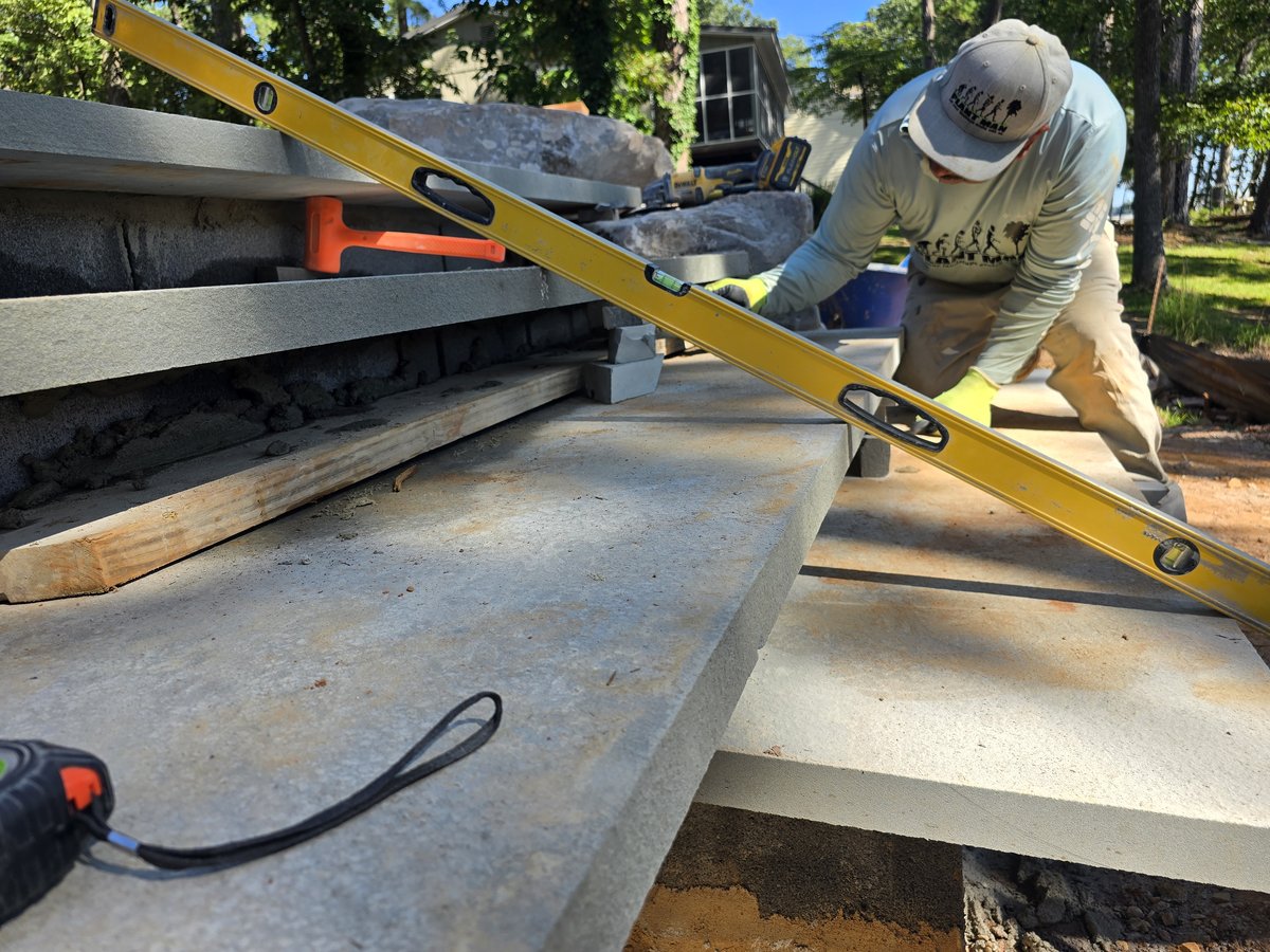 Elton laying and leveling concrete steps under construction, boulders staged beyond