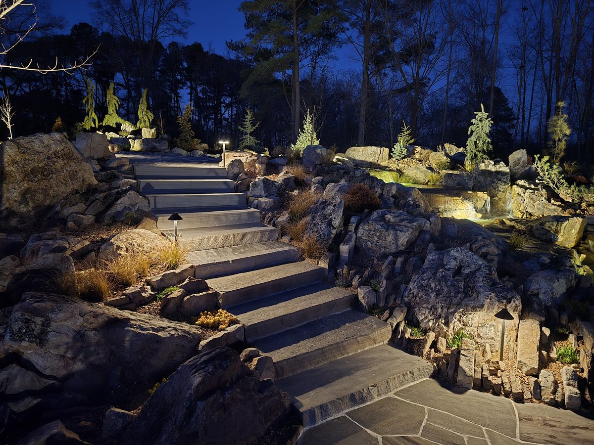 Path lighting along stone steps with an illuminated waterfall beyond