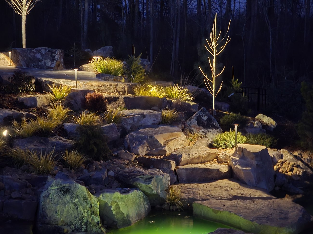 Terraced boulders and plantings lit at night beside a pond