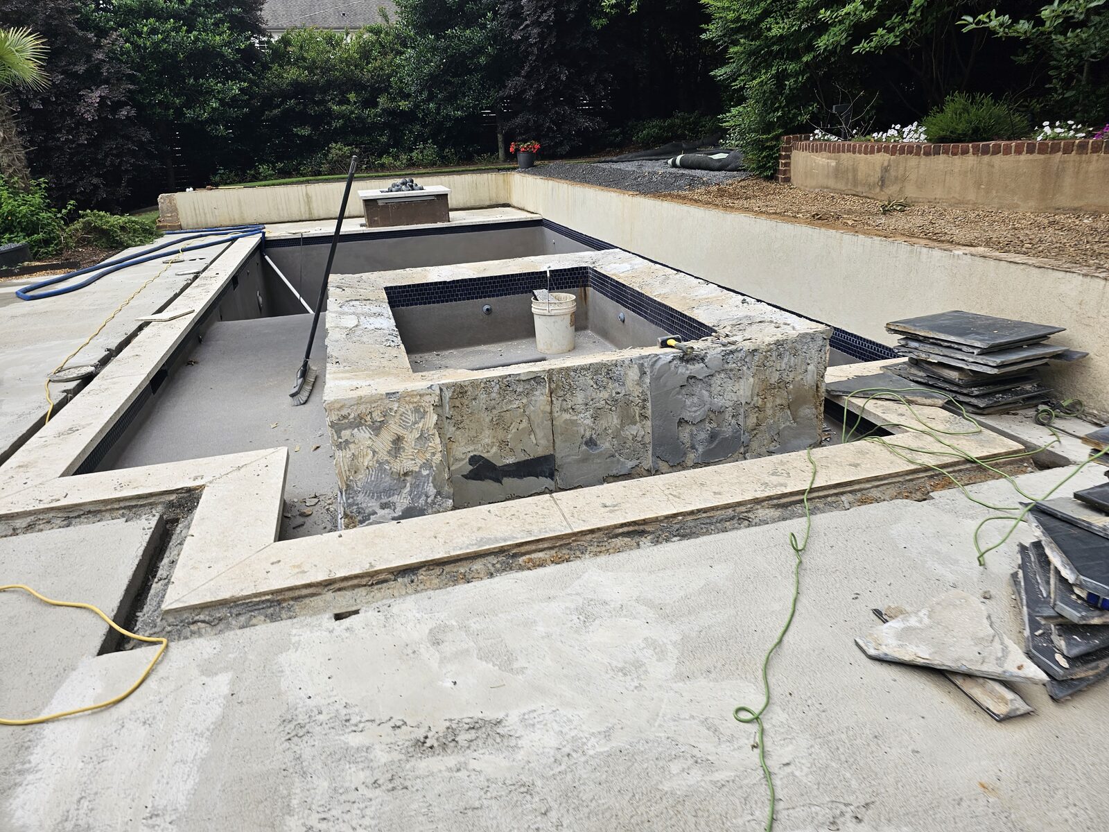 The pool and spa shell stripped to bare concrete during the rebuild, with new dimensional stone coping staged nearby