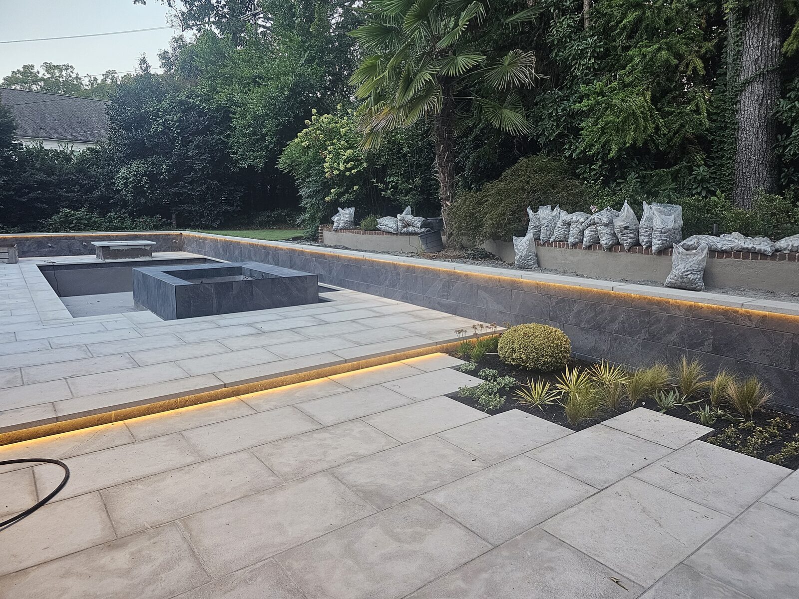 Wide dusk view of the finished pool, spa, and Ipe bench, with recessed lighting glowing along the walls