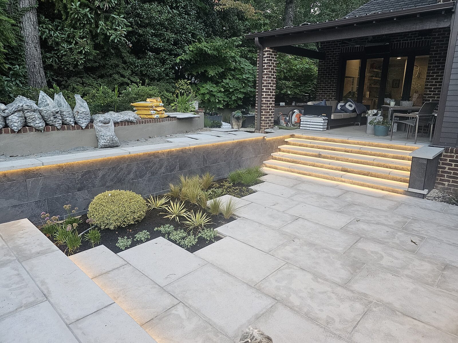The floating limestone planter steps and patio underlit at dusk, with the covered porch glowing beyond