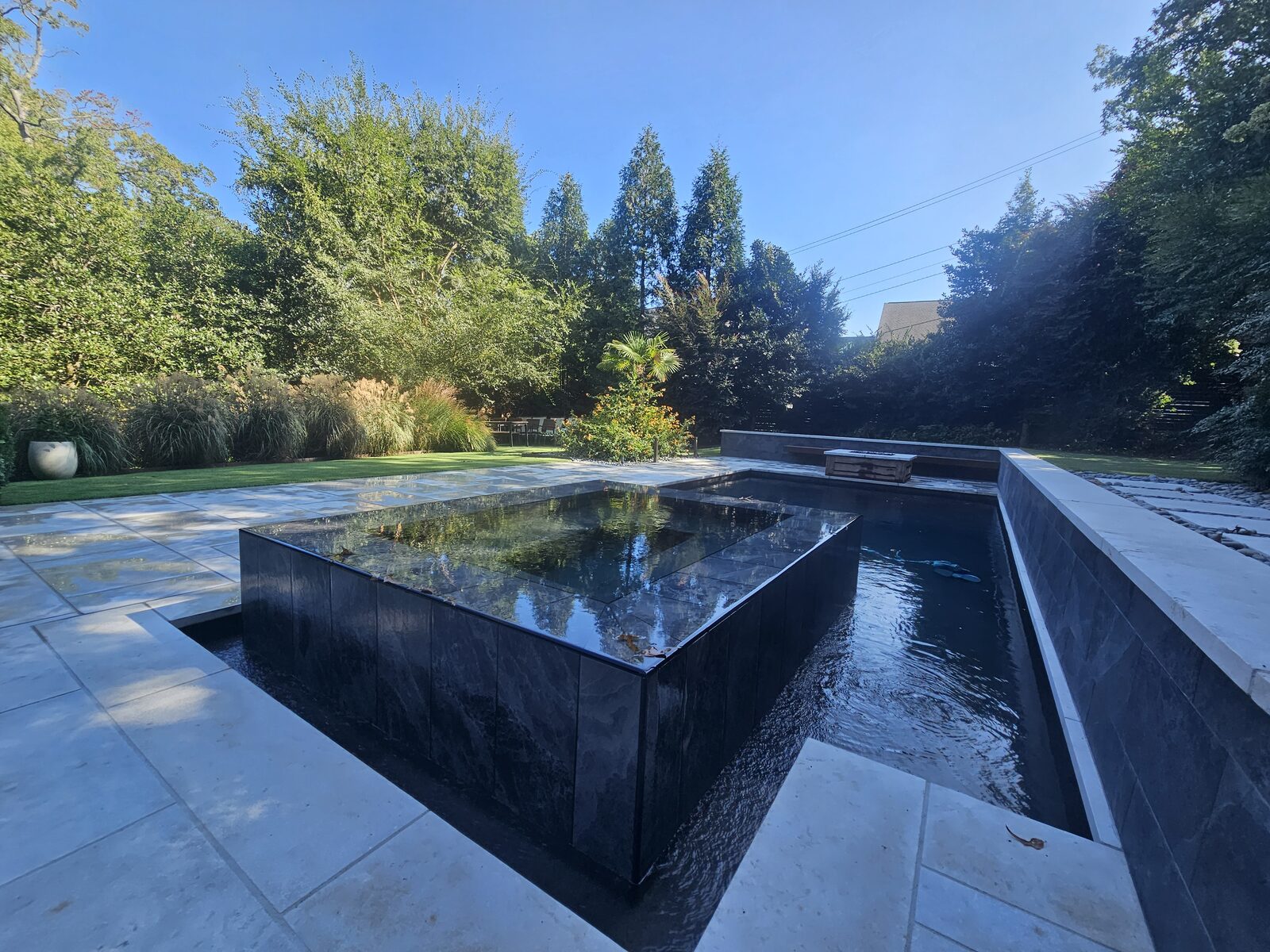 The finished pool and spa seen from the corner of the patio in daylight, with the floating Ipe bench along the wall