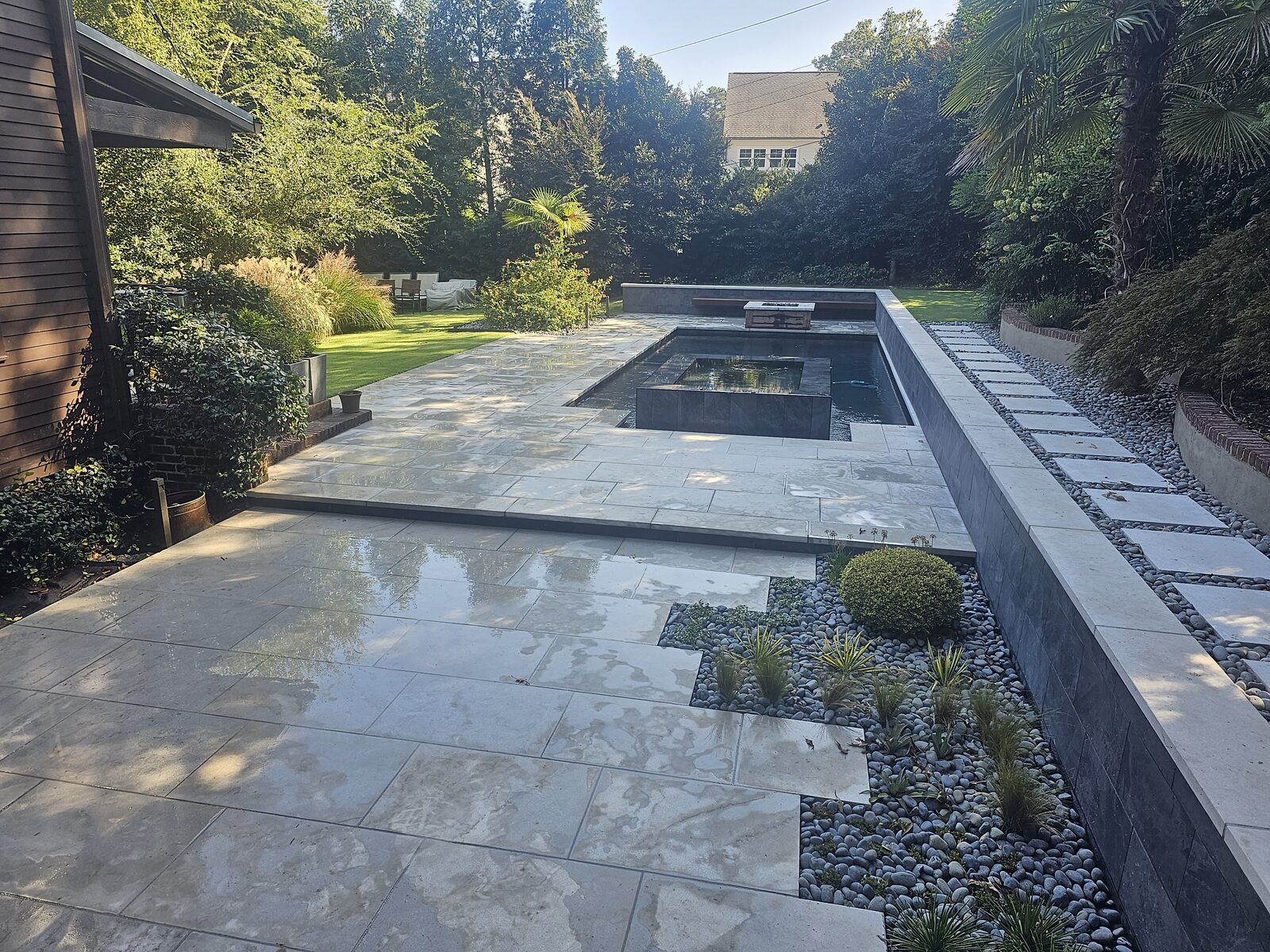 Wide daylight view of the finished pool and spa's black slate vanishing edge and limestone patio