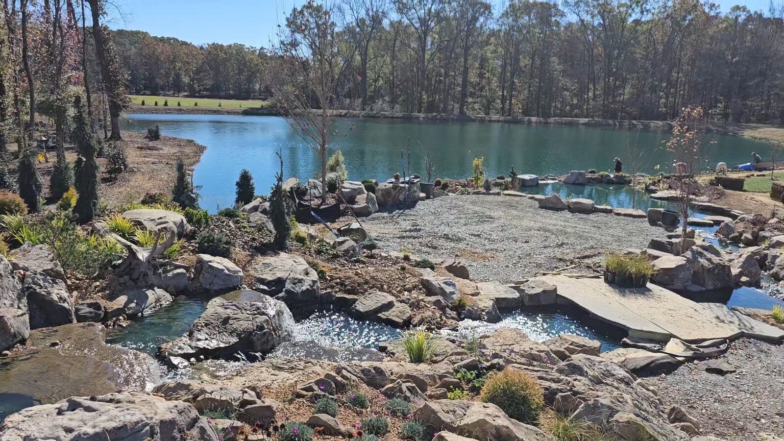 Aerial view of the property mid-construction, showing the recreation pond and boulder waterfall taking shape beside the private lake
