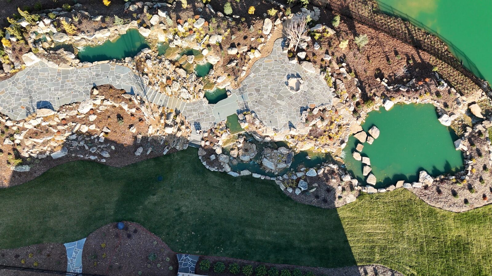 Aerial view of the finished water feature, stone patios, and recreation pond connecting to the private lake