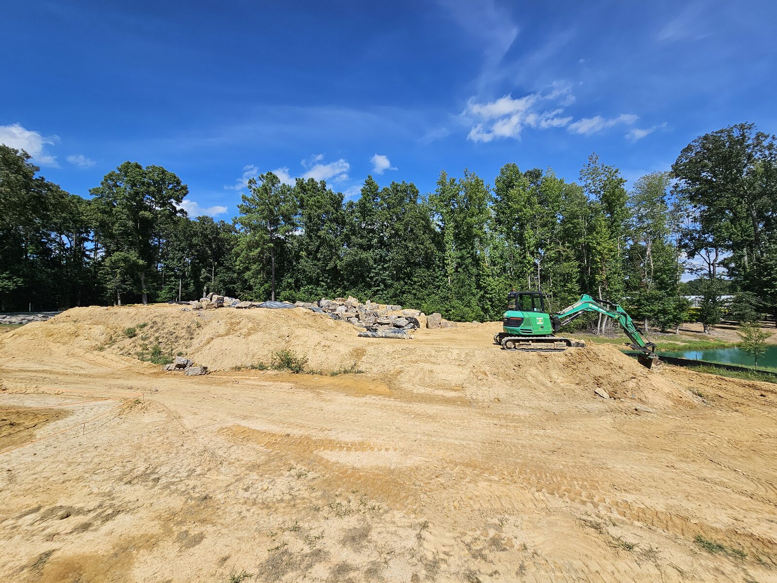 An excavator placing boulders onto the graded berm during early construction of the waterfall