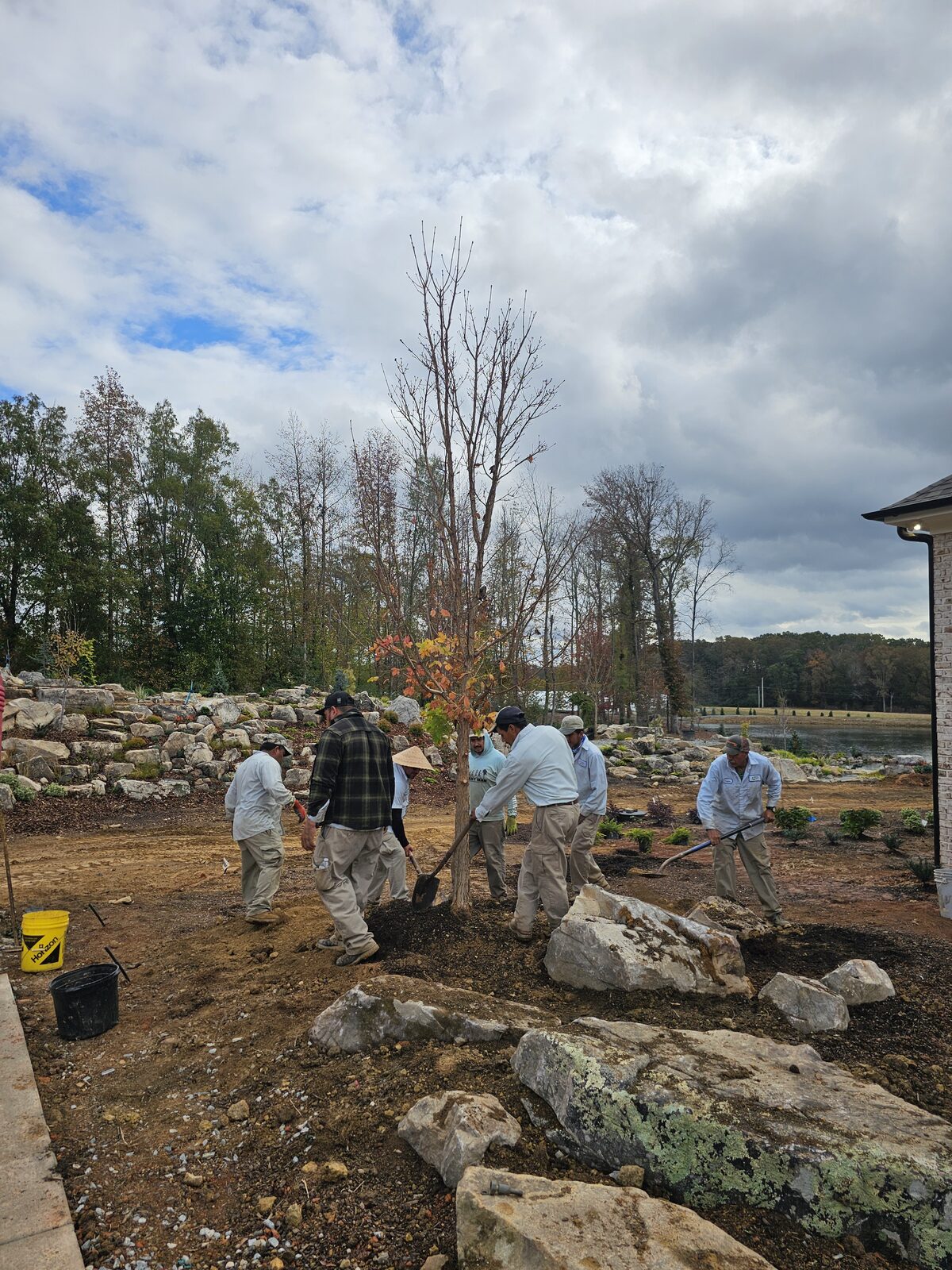 The Plant Man crew planting a tree amid the finished boulder waterfall and stone steps, fall color in the trees