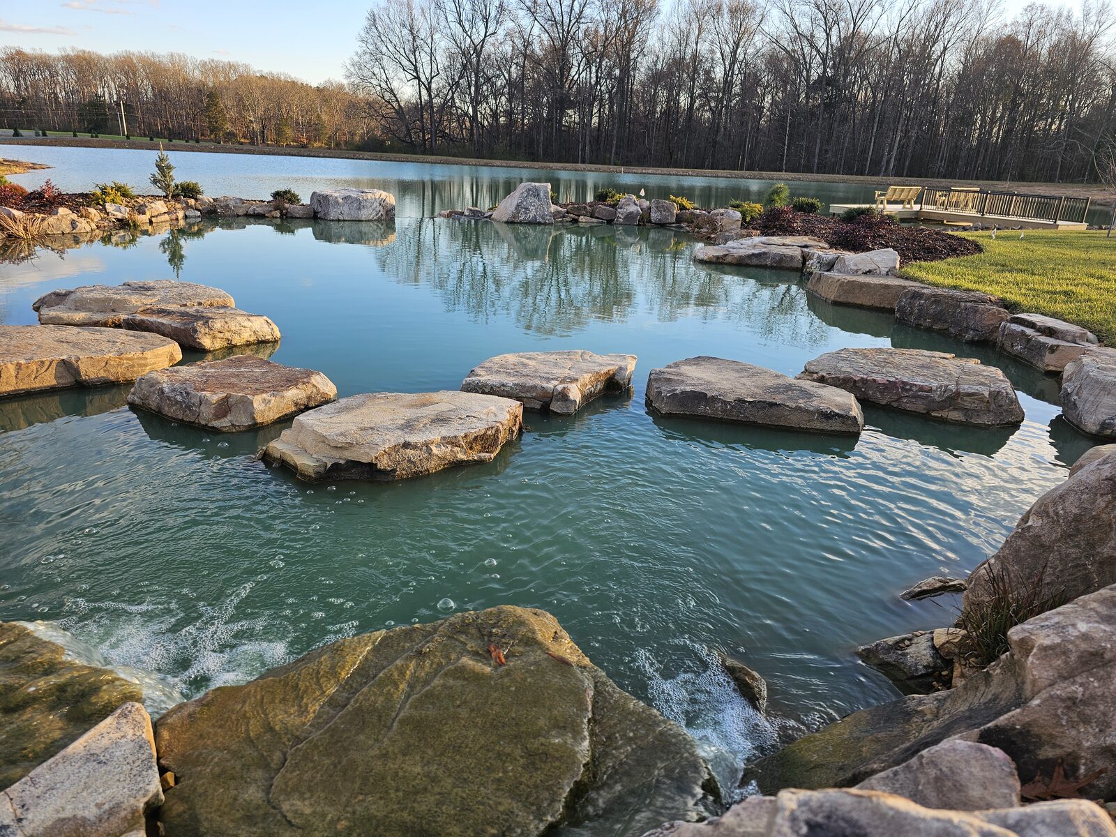 Stepping stones crossing the recreation pond at golden hour, with a dock visible on the private lake beyond