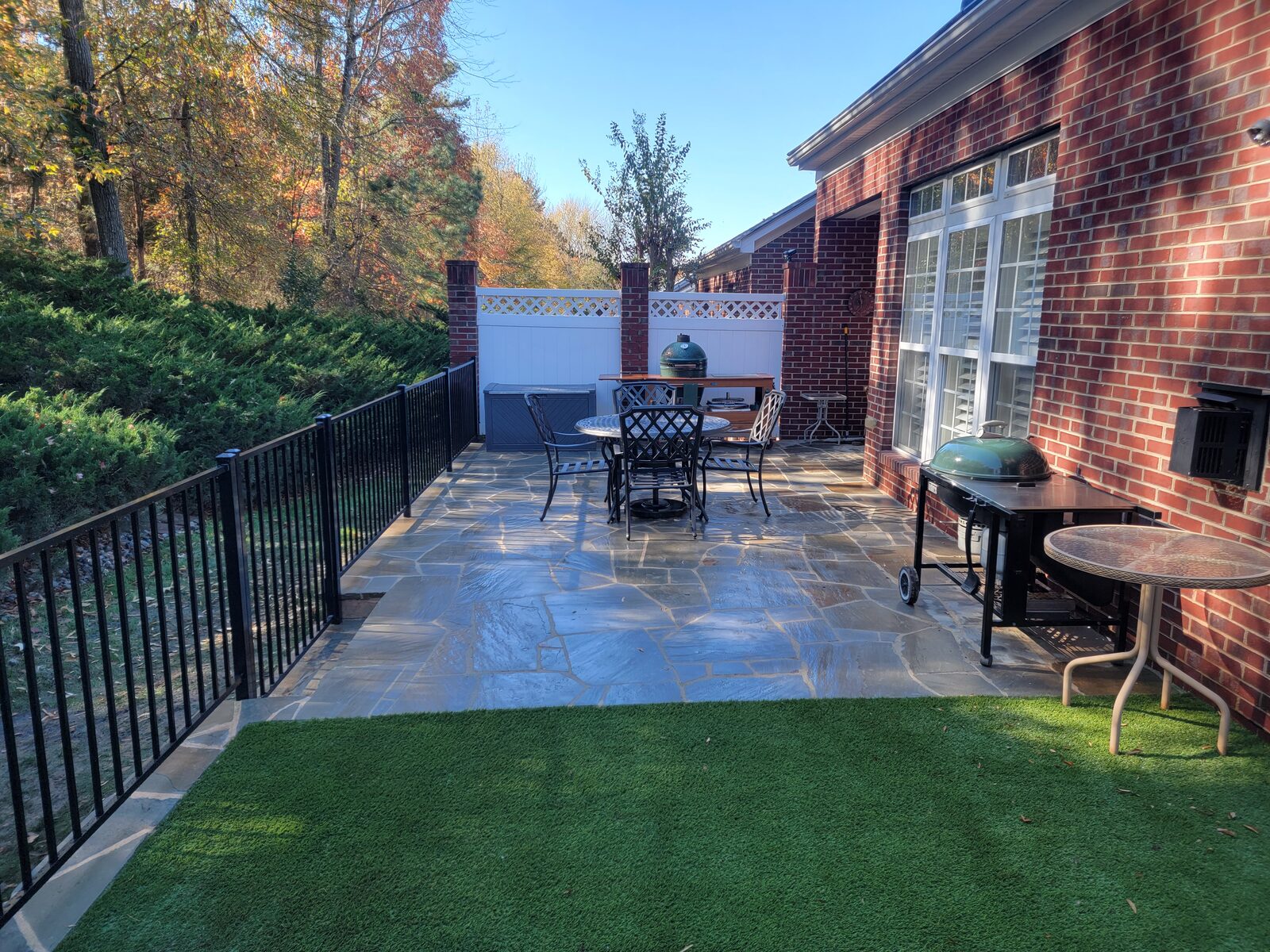 A flagstone patio off a screened porch, with a dining table, grill, and artificial turf lawn