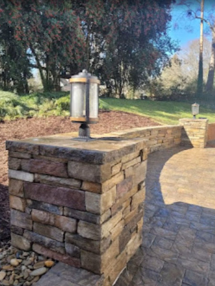 Paver walkway beside a stacked-stone pillar with a lantern-style light fixture