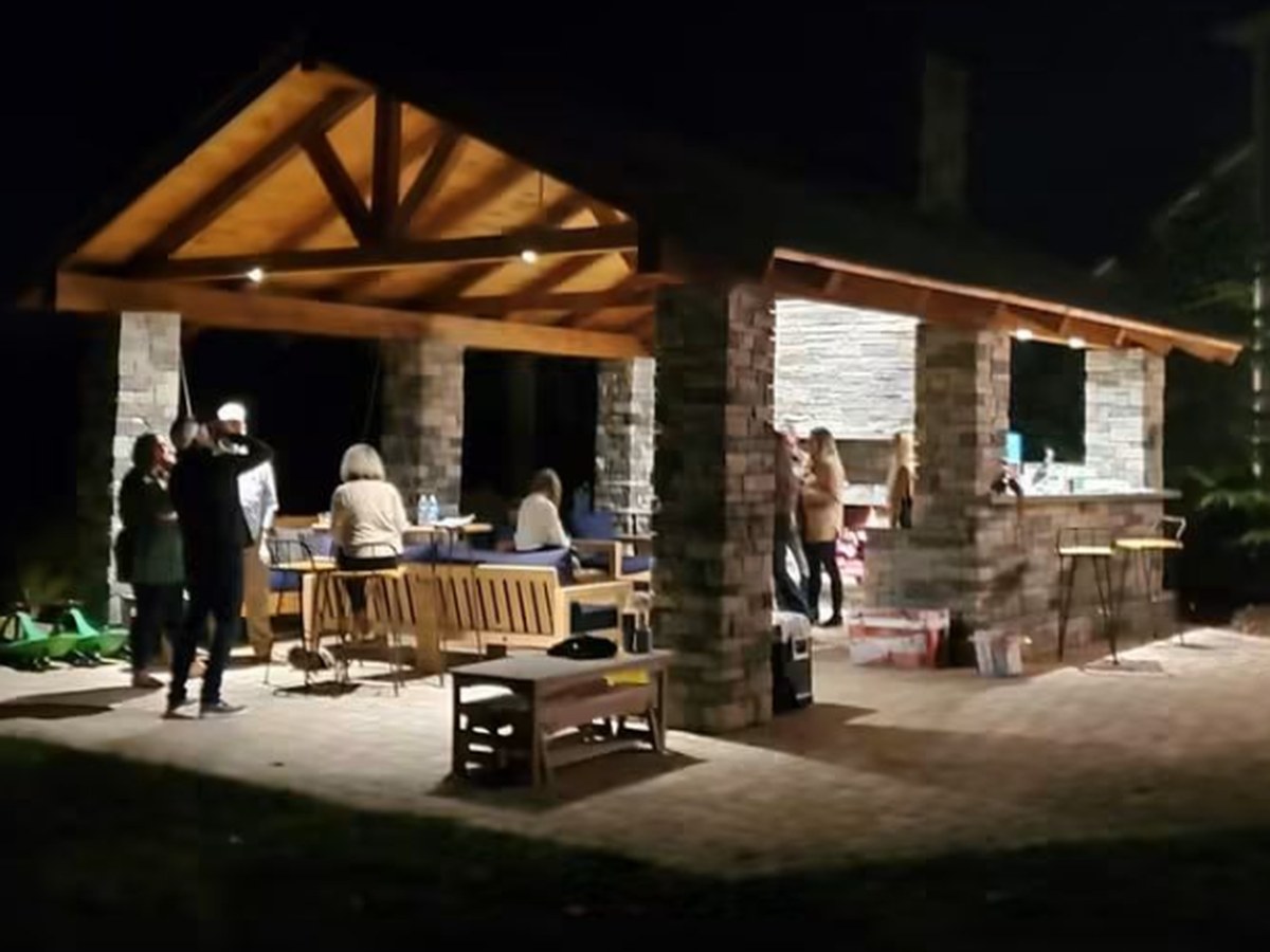 Complete timber-framed pavilion with stone columns and an outdoor kitchen bar, lit and in use at night