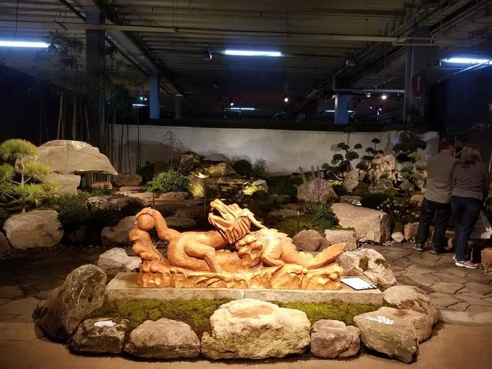 A sculptural dragon fountain set among boulders and bonsai pines in a temporary show garden