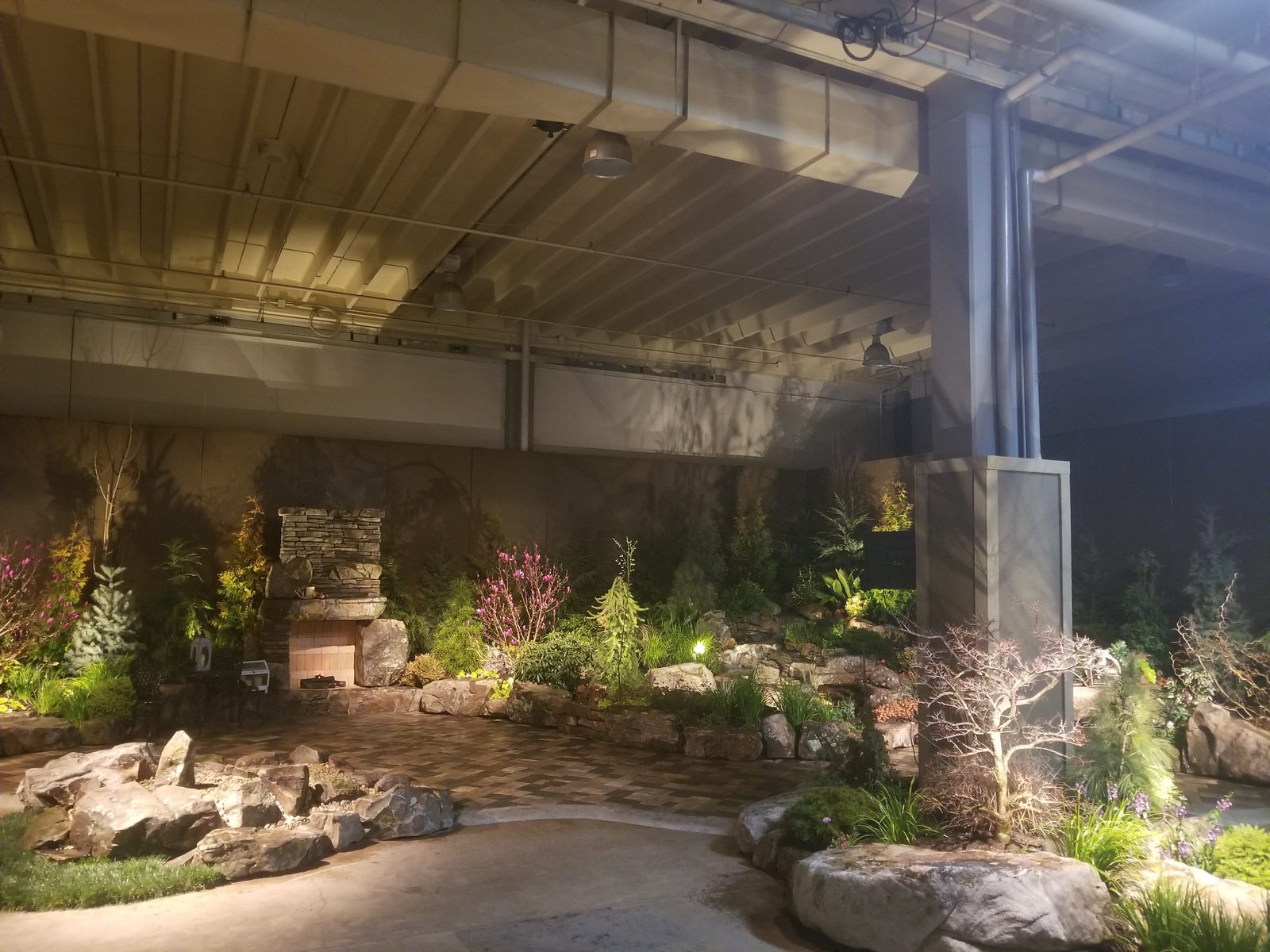 A temporary show garden with a lit stacked-stone fireplace, boulder-lined patio, and layered planting