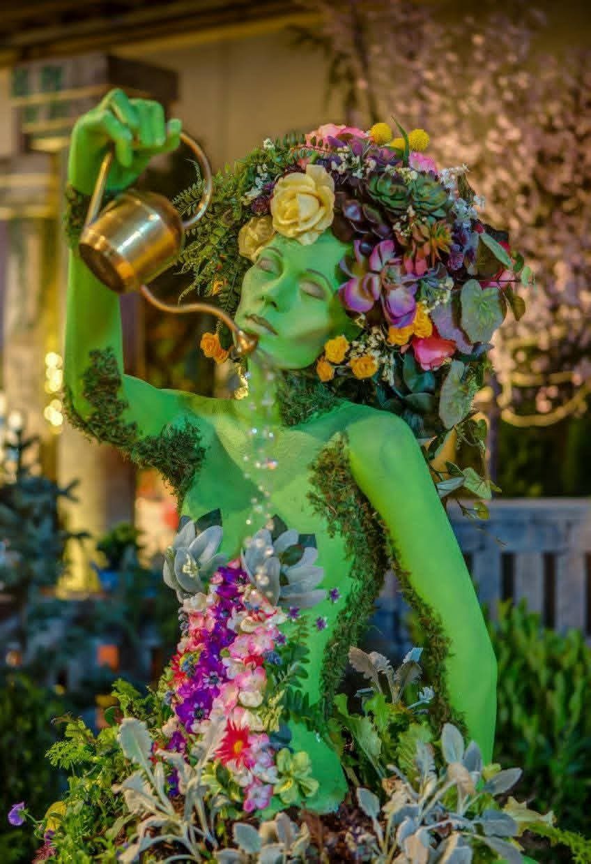 A living nature-spirit figure covered in moss, succulents, and flowers, part of a themed garden display