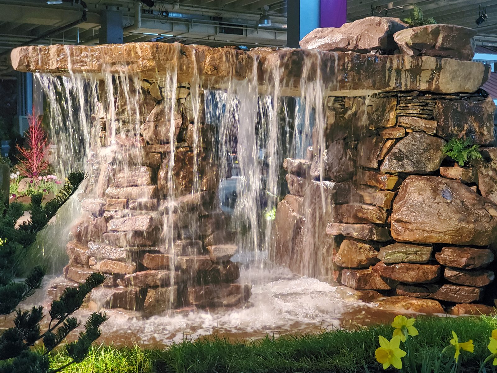 A dramatic sheet waterfall cascading through a stacked-stone wall, built as a temporary water feature
